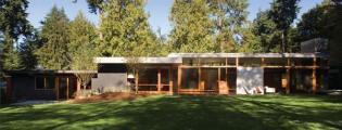 Glass walls, blackened steel, and teak plywood cabinets let this mid 20th century home in a Seattle suburb blend with its leafy surroundings.