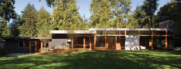 Glass walls, blackened steel, and teak plywood cabinets let this mid 20th century home in a Seattle suburb blend with its leafy surroundings. 
