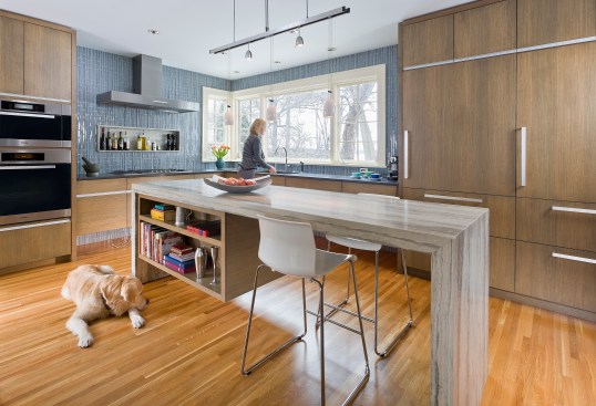 Modern kitchen with rift sawn white oak cabinets and large stone island with woman and dog