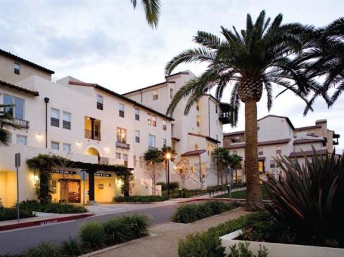 Articulated cast stone, wood-and-wrought iron balconies, and tile roofs share the architectural character of an adjacent historic village. The at-grade entrance to each two-level parking garage is obscured by walk-up townhouses accessed from the street.
