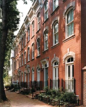 Venetian-style town houses with traditional stoops line a street adjacent to a downtown park.