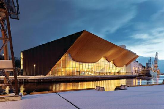 The+geometric%2c+dark-gray+aluminum+panels+cladding+the+building%27s+rear+and+side+elevations+juxtapose+the+warmth+and+curves+of+the+Kilden+Performing+Arts+Center%27s+main+facade%2c+which+emulates+a+rippling+stage+curtain+or+the+wooden+hulls+of+ships+pulling+into+harbor.