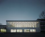The exterior incorporates an aluminum rainscreen from Kalzip and a curtainwall from Schüco. Ecker describes the existing 11-building, 1960s complex as “well-built, but quiet,” in an aesthetic worth respecting. “We found that we could reinterpret that on the outside,” Ecker says. Visible through the high-efficiency glass from Glas Trösch is the main assembly hall and its three rotationally cast concrete columns that support the mass of the concrete ceiling.