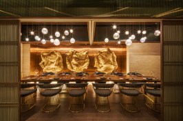 A private dining space offers tables and chairs by Champion Design + Furniture, before a custom art piece of brass-finished wire mesh, which pays homage to the shape of oysters.