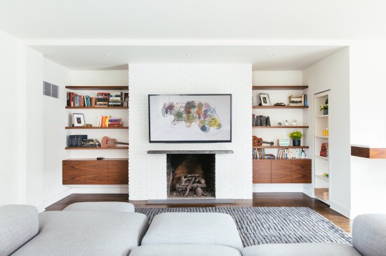 Brick clad fireplace is flanked with floating walnut cabinets and shelves; clean Pennsylvania bluestone hearth and mantel mark the working woodburning fireplace