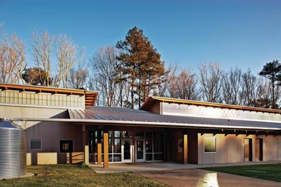 The entrance is located strategically on the building's northwest fa?ade. A double-height glazed wall opposite the front door frames a view down to the pond. To the left of the entrance is a corrugated rainwater cistern, fed by a gutter system that channels roof runoff. The water collected is used primarily for site irrigation.