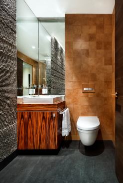 Sleek rosewood veneer, rough stacked basalt walls, basalt floor tile, and leather wall tiles make for a deluxe powder room that’s a collage of warm and cool materials. Project: Mountain Villa Residence, Austin, Texas; Architect/Interior Designer: Ulrich Dangel and Tamie Glass, Austin, Texas; Builder: Branson Fustes, Pilgrim Building Company, Austin, Texas.