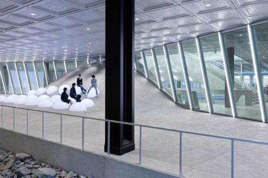 A grid of recessed downlights in the plaza’s pressed tin ceiling illuminates the indoor-outdoor space. To increase the vertical light levels and create more visual interest at this main pedestrian thoroughfare, linear-lensed LED fixtures are integrated into the storefront mullions. Translucent seating pods on the “bump” are internally illuminated with color-changing LEDs.