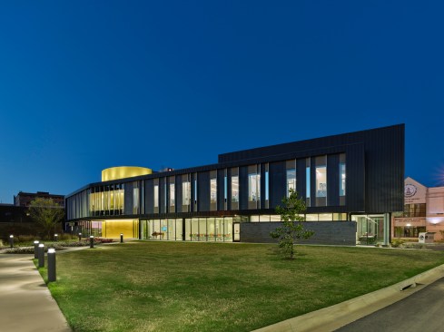 A bold oval shaped cylinder housing utilitarian functions becomes the hinge point for the bending form, and a visual marker of entrance from the surrounding parking and streets.