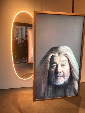 A photo of Philippe Starck in front of his La Plus Belle lighted mirror for Flos.
