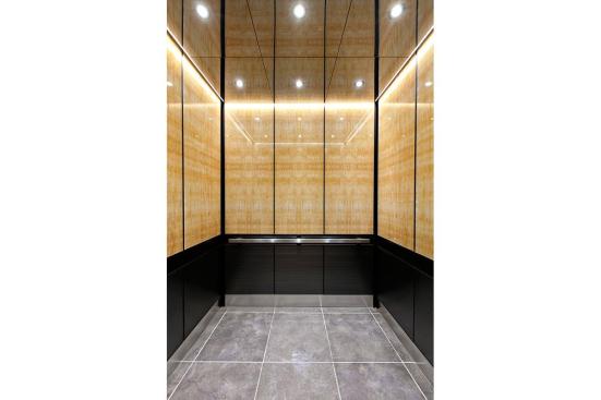 LEVELe-105 Elevator Interior with upper panels in ViviStone Honey Onyx, Standard finish; lower panels in Fused Graphite, Sandstone finish, Dallas pattern; Handrail panel in Fused Graphite, Seastone finish; Quadrant Handrail in Satin Stainless Steel; Elevator Ceiling in Fused Nickel Silver, Mirror finish at 176 Broadway, New York, New York