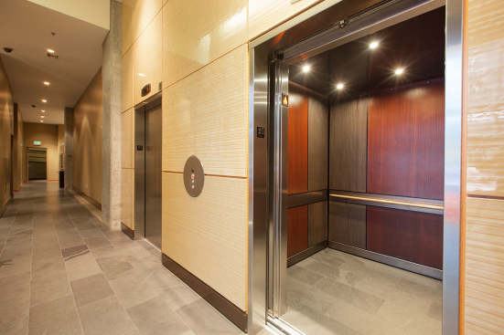 LEVELe-105 Elevator Interior with main panels in Bonded Bronze with Dark Patina and Rain pattern; accent panels in custom wood veneer; handrail panel in Fused Nickel Silver with Sandstone finish; Round handrail in Stippled Bronze at The Wyatt, Portland, Oregon