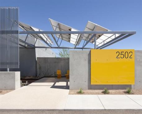 The entry features concrete and steel with a solar array that provides shade.
