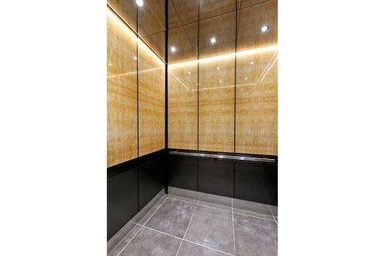 LEVELe-105 Elevator Interior with upper panels in ViviStone Honey Onyx, Standard finish; lower panels in Fused Graphite, Sandstone finish, Dallas pattern; Handrail panel in Fused Graphite, Seastone finish; Quadrant Handrail in Satin Stainless Steel; Elevator Ceiling in Fused Nickel Silver, Mirror finish at 176 Broadway, New York, New York