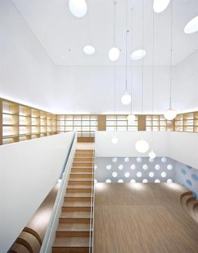 In+the+library%2c+wood+flooring+from+Armstrong+lends+warmth+to+the+white+double-height+space.+Circular+windows+on+the+lower+level+look+out+into+one+of+many+courtyards%2c+and+terraced+seating+areas+provide+gathering+spaces+for+the+children.