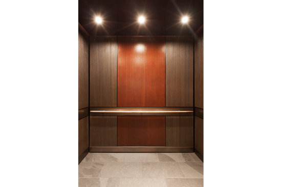 LEVELe-105 Elevator Interior with main panels in Bonded Bronze with Dark Patina and Rain pattern; accent panels in custom wood veneer; handrail panel in Fused Nickel Silver with Sandstone finish; Round handrail in Stippled Bronze at The Wyatt, Portland, Oregon