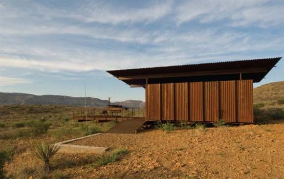Practical, impervious, and low-tech, the cargo-container guest cabins are at home on the harsh Texas range. The five containers three bedrooms, a kitchen, and storage space are linked by a deck of steel bar grating with built-in bench and barbecue.