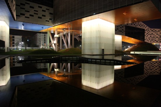Looking at the center across the water feature beneath it, at night.