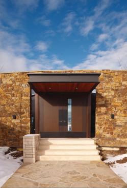 The entry doors’ wenge background echoes the interior cabinetry, and bronze-colored steel panels reflect the house’s exposed structural steel, light fixtures, and handrails.