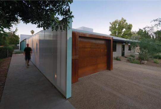 The garage front's rusted steel facing contrasts with the smooth polycarbonate panels of the garden wall.