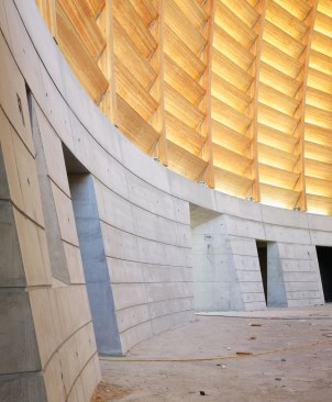 The interior space is defined by a curving, arcing wall of fixed wooden louvers, which give off a warm glow when illuminated by the sun.