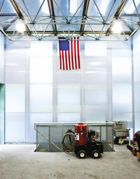 The main interior space is an 800-square-foot ground level garage and workroom. Daylight filters in through the skylights and the white polycarbonate walls, reducing the need for interior lighting. A staircase leads down to the 400-square-foot basement level that houses the heat pumps and other mechanical systems.