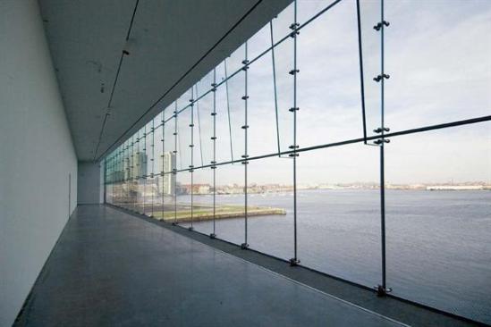Founder's Gallery The Founder's Gallery is a crossover space that spans the full width of the building's north face. By connecting the main east and west galleries, the linear room is woven into the choreography of the art-viewing sequence. The gallery's glass curtain wall-which stretches floor to ceiling, revealing a panoramic view of Logan Airport, Bunker Hill, and Boston's business district-is composed of cantilevered laminated glass fins with point support fittings. The wall was designed and tested in a full-scale mock-up to ensure its ability to withstand high winds whipping in from the Atlantic Ocean.