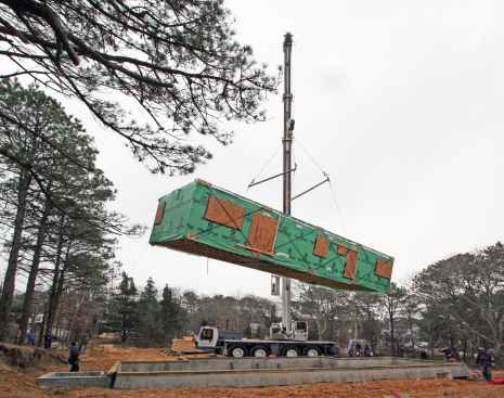 Prefab modules being set by crane atop the site-built foundation.