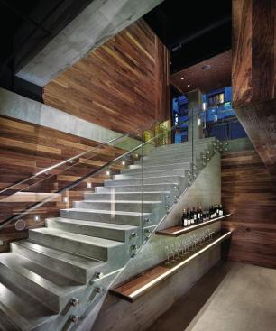 The main staircase provides access from the ground-floor reception/retail space down to the tasting and tapas areas of Press Club. Walnut shelves (with inset LED strips to light the labels) showcase some of the bottles that can be tasted at the different winery stations. STEP LIGHTS - Winona LED - Step 02 Square Deco step lights - winonalighting.com - WOOD PANELING - Plant Architectural Woodwork - American black walnut - plantwoodwork.com - STAIR RAIL ASSEMBLY - Eclipse Design - Custom stainless steel and glass stair rail - eclipsedesigngp.com