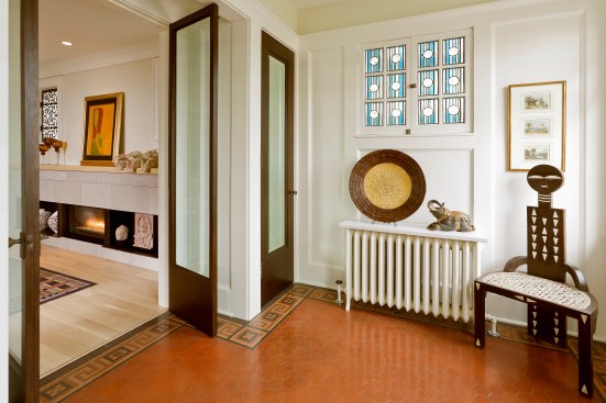 Entryway of home with tile and mosaic floor and view through doors into living room and fireplace
