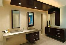 The room's dark Wenge wood cabinets and backlit canopies provide a stark contrast to the muted beiges and grays of the bath's slip-resistant porcelain tile and fireslate countertops, sinks, and benches. The fixtures and fittings were chosen for their simp