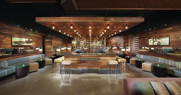 The tapas bar is the only place where wines from multiple wineries can be purchased. Framed by custom banquettes and with an events lounge tucked behind a wall-sized wine rack, this, the third of three main bar areas, is kept quiet enough for conversation with acoustic fabric lining the unfinished ceiling above the decorative soffits. BANQUETTE FABRIC - Maharam - Repeat Classic fabric - maharam.com - DECORATIVE LIGHT FIXTURES - Resolute - Clarity Ceiling fi xtures - resoluteusa.com - STOOL AND OTTOMAN UPHOLSTERY FABRIC - Architex - Voila upholstery fabric in Mushroom - architex-ljh.com - BARSTOOLS - ISA International - 1292 Cube barstool - haveaseat.com - TRACK LIGHTING - Translite Sonoma - Micro Spot G - translite.com