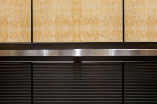 LEVELe-105 Elevator Interior with upper panels in ViviStone Honey Onyx, Standard finish; lower panels in Fused Graphite, Sandstone finish, Dallas pattern; Handrail panel in Fused Graphite, Seastone finish; Quadrant Handrail in Satin Stainless Steel at 176 Broadway, New York, New York