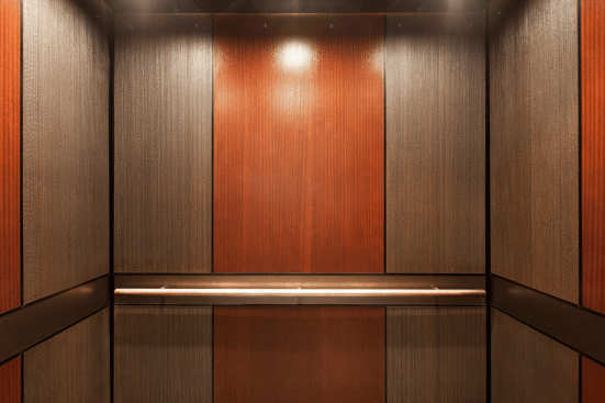 LEVELe-105 Elevator Interior with main panels in Bonded Bronze with Dark Patina and Rain pattern; accent panels in custom wood veneer; handrail panel in Fused Nickel Silver with Sandstone finish; Round handrail in Stippled Bronze at The Wyatt, Portland, Oregon