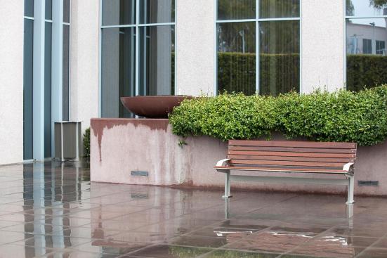 Knight Bench shown in 6 foot, backed configuration with Aluminum Texture powdercoated frame, FSC Pure Ip? hardwood slats and two armrests, and Knight Litter Receptacle with Slate Texture powdercoat at Mission City Corporate Center, San Diego, California