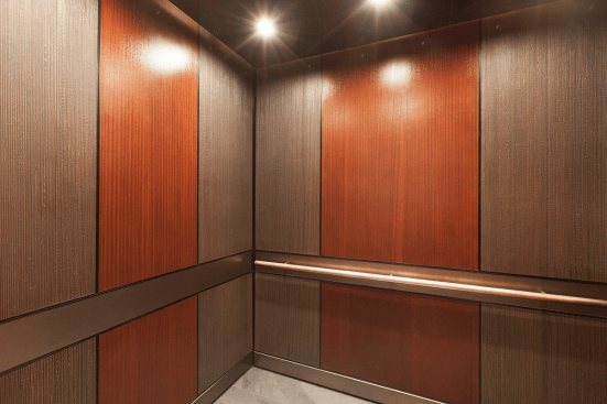 LEVELe-105 Elevator Interior with main panels in Bonded Bronze with Dark Patina and Rain pattern; accent panels in custom wood veneer; handrail panel in Fused Nickel Silver with Sandstone finish; Round handrail in Stippled Bronze at The Wyatt, Portland, Oregon