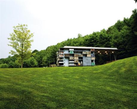 The barn's space-frame roof projects out over a paved area, providing a shelter for the storage of sand and other materials. An outdoor shower is a water source for wetting materials and a place for the owner's family to rinse off after taking a dip in the nearby lake.