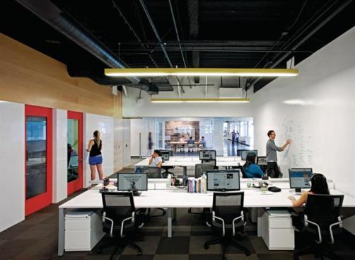 An+open-office+suite%2c+with+conference+rooms+and+enclosed+offices+lining+one+wall%2c+and+an+expansive+white+board+surface+on+the+other.