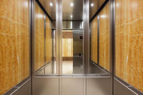 CabForms Series 2000-N Elevator Interior with upper inset panels in ViviStone Honey Onyx, Pearlex finish; lower inset panels in Stainless Steel, Linen finish; stiles and rails in Stainless Steel, Seastone finish; Sextant Handrail in Stippled Stainless Steel at the Woolworth Building, Eugene, Oregon