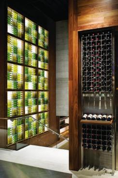 Empty wine bottles backlit by LED fixtures form a sculptural feature wall at the top of the main staircase that leads to the tasting bars. The empty bottles are complemented by full ones in the nearby retail display, which was designed and fabricated by Eclipse Designs. WALLCOVERING - Jelinek Cork Group - Fabric Cork - jelinek.com - WALL SURFACING - Giampolini & Co. - Boardformed cement plaster - giampolini.com - DISPLAY LIGHTING - Winona LED - LED display lighting - winonalighting.com