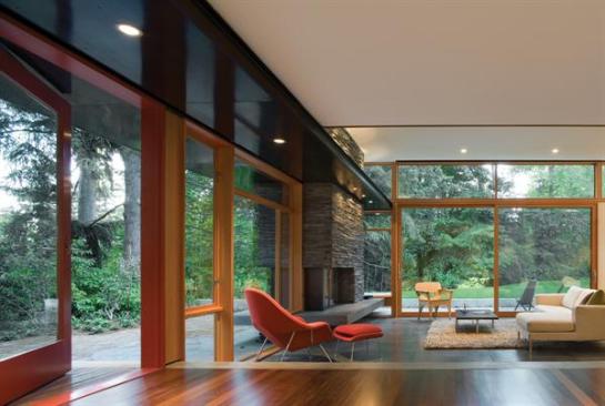 Glass walls, blackened steel, and teak plywood cabinets let this mid 20th century home in a Seattle suburb blend with its leafy surroundings. The new skylighted entry ends at the open kitchen living area and a pivoting door to the garden.