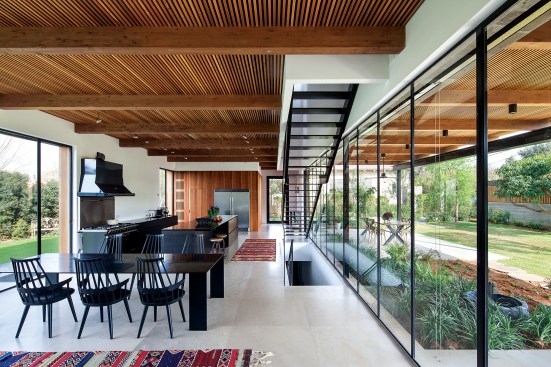 The ground floor of the house contains the kitchen as well as dining and living spaces. The wood-slat ceiling continues outside to the south to form a pergola that shields open-air seating and dining areas from the elements.