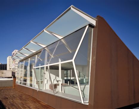 A floating staircase, with triangulated treads for strength, rises from the ground-floor office to a transparent penthouse and deck.