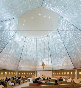 The chapel’s double wall (solid on the exterior and punched with a repeating pattern of holes on the interior) is capped with a halo-shaped skylight between the two surfaces, which provides general, filtered illumination through the scrimlike perforated metal screens during the day. 