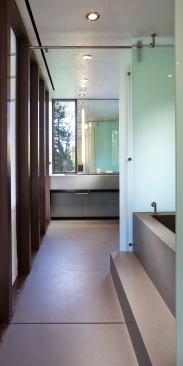 Engineered stone forms the floor, tub, and wainscot of this master bath, which doubles as a pool cabana. Sliding glass partitions at the tub yield a variety of possible configurations.