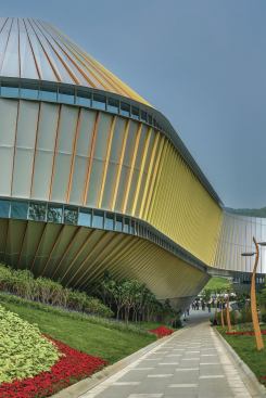 A path leading past a yellow-accented section of one of the structures, with exterior planting displays on either side. 